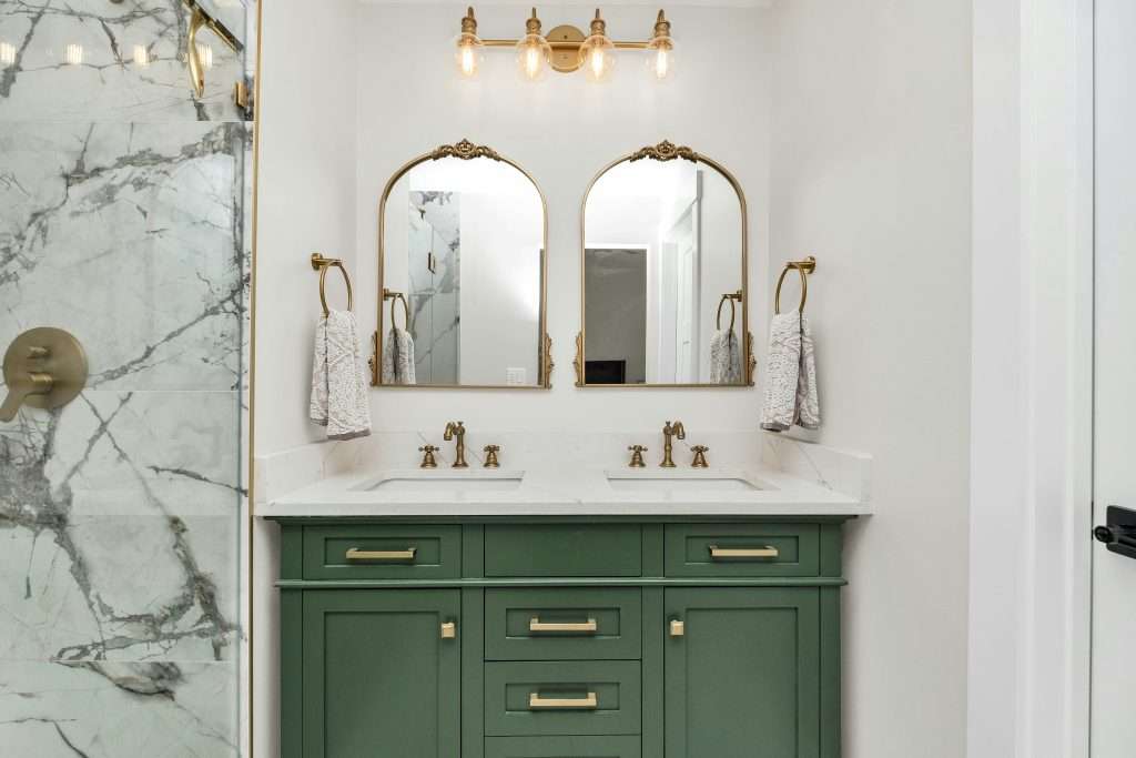 Finished bathroom remodel featuring a green double vanity with gold fixtures, marble countertop, and marble shower tile