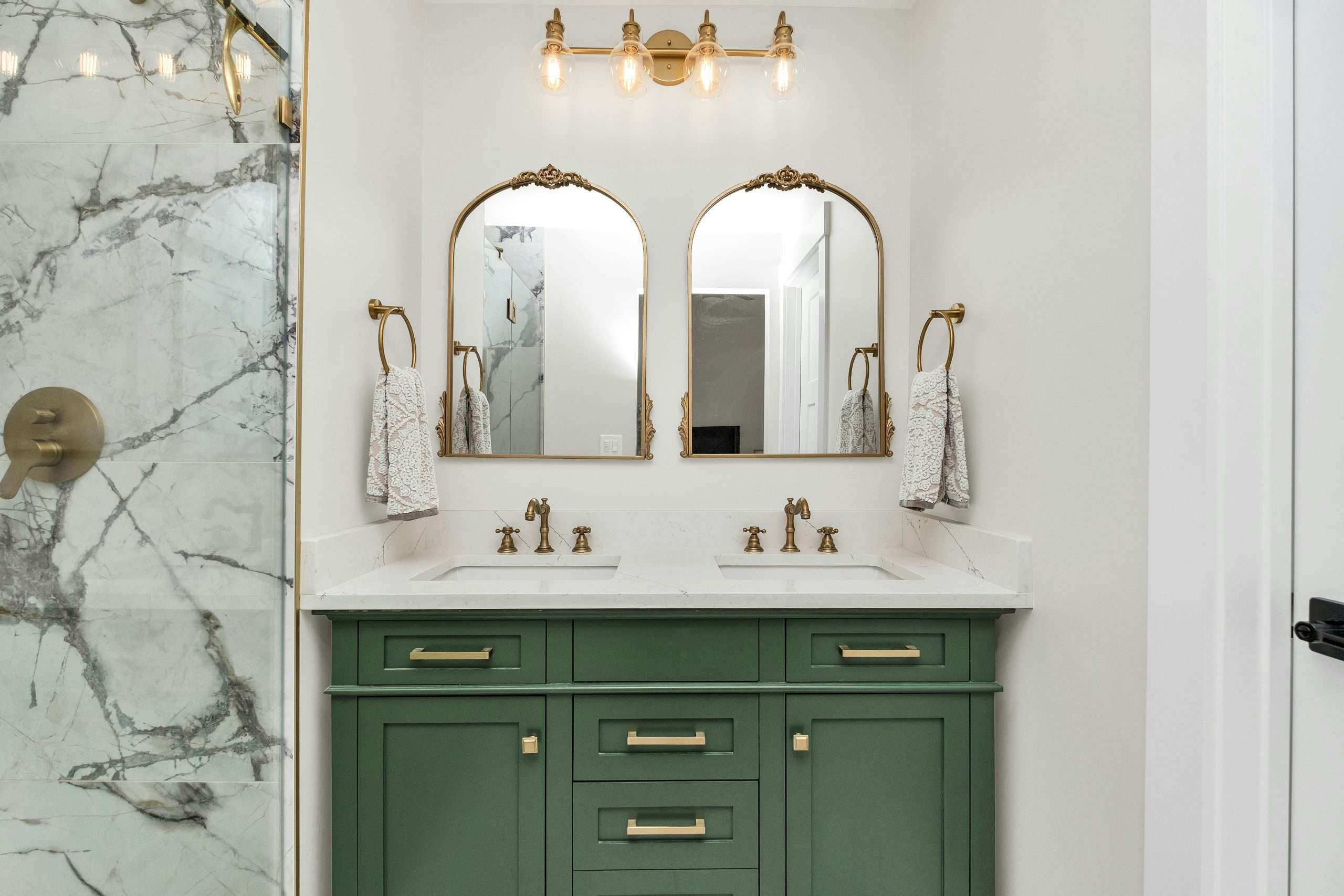 Finished bathroom remodel featuring a green double vanity with gold fixtures, marble countertop, and marble shower tile