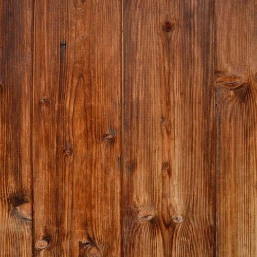 A close-up view of several vertical wooden planks with a warm brown finish. The wood grain, knots, and texture are clearly visible, giving the surface a rustic and natural appearance.